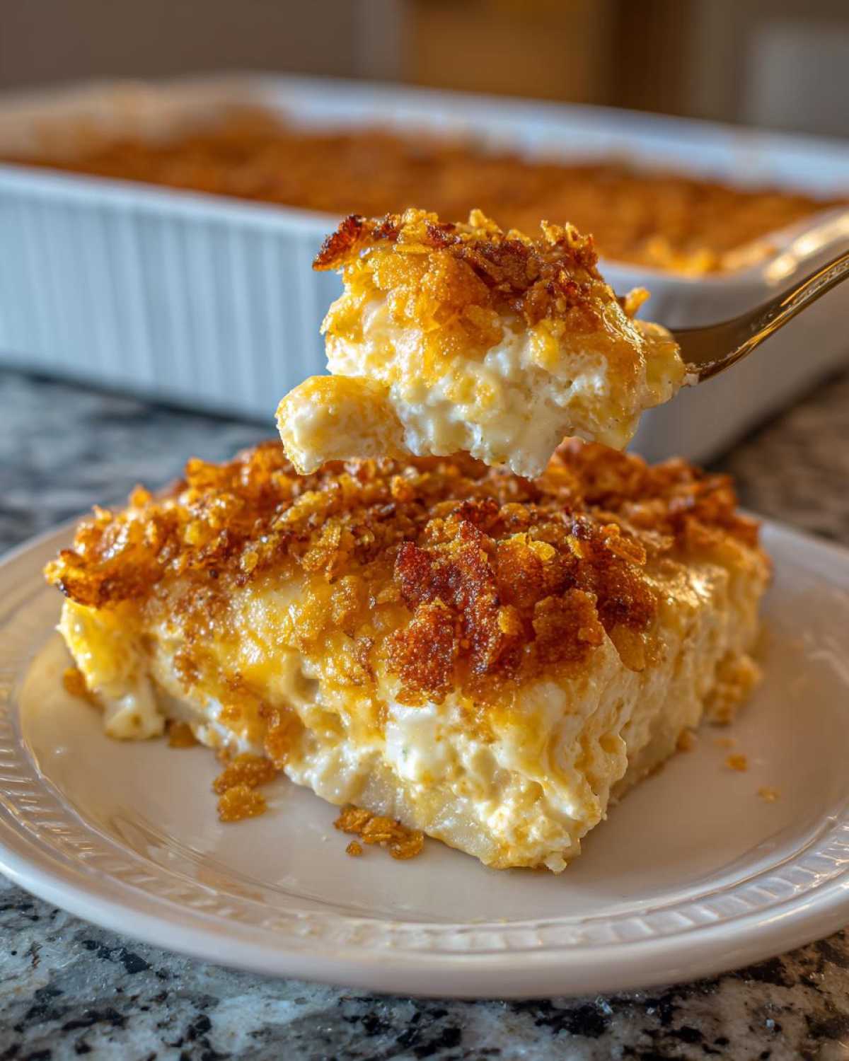 A spoonful of creamy potato casserole with a golden, crunchy topping being lifted from a slice on a white plate.