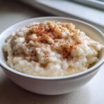 Close-up of a white bowl filled with creamy rice pudding recipe, dusted generously with cinnamon.