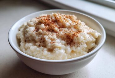 Close-up of a white bowl filled with creamy rice pudding recipe, dusted generously with cinnamon.