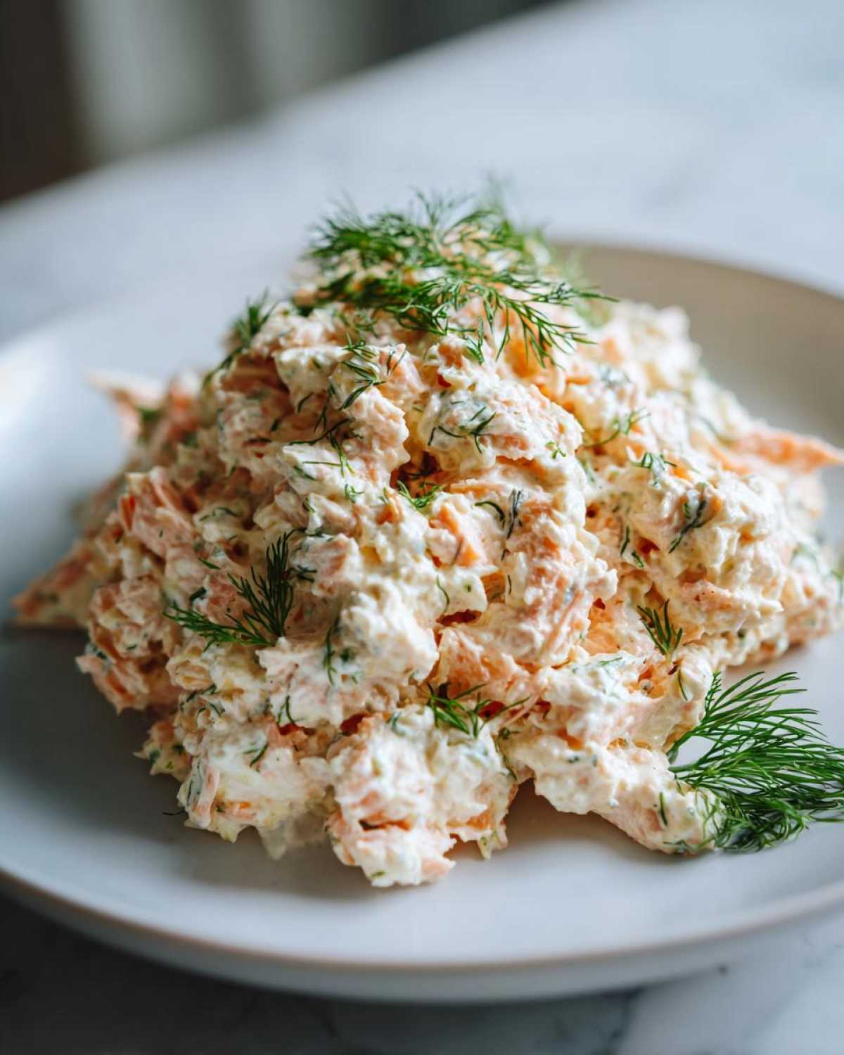 A mound of creamy salmon salad mixed with herbs and topped generously with fresh dill sprigs.