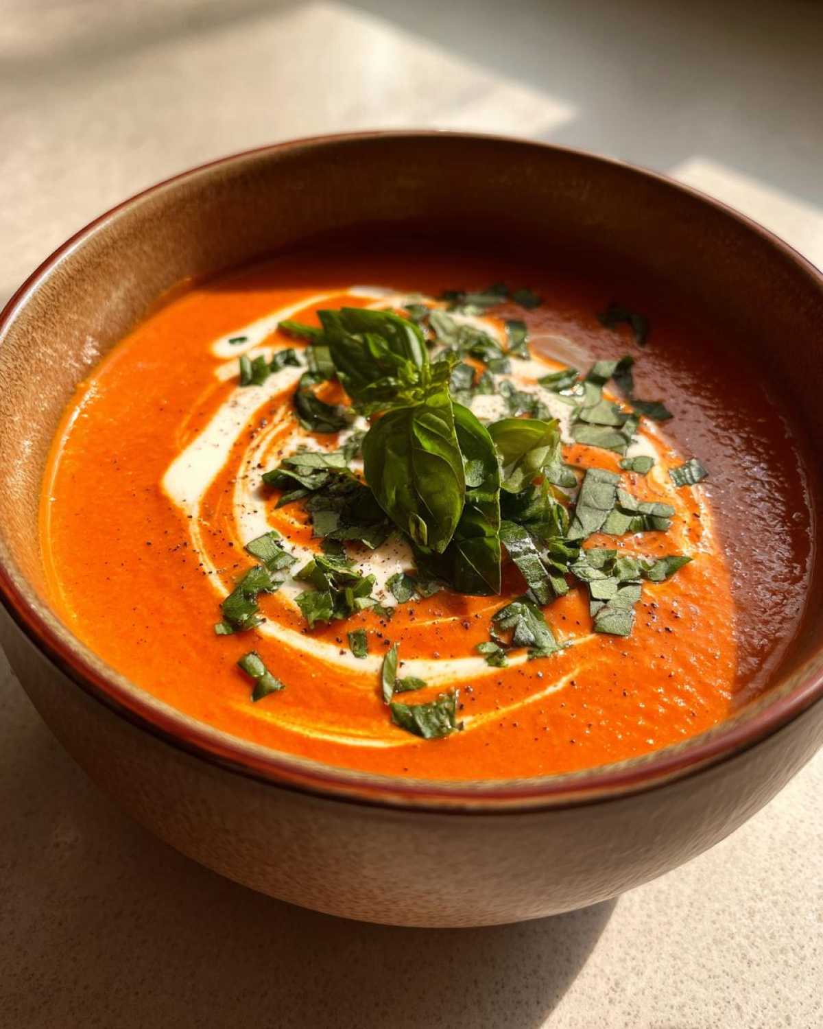 Close-up of a rich, orange-red tomato bisque garnished with a swirl of cream and fresh, chopped basil.