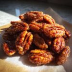 A close-up mound of glistening, freshly made candied pecans coated in a sugary glaze.
