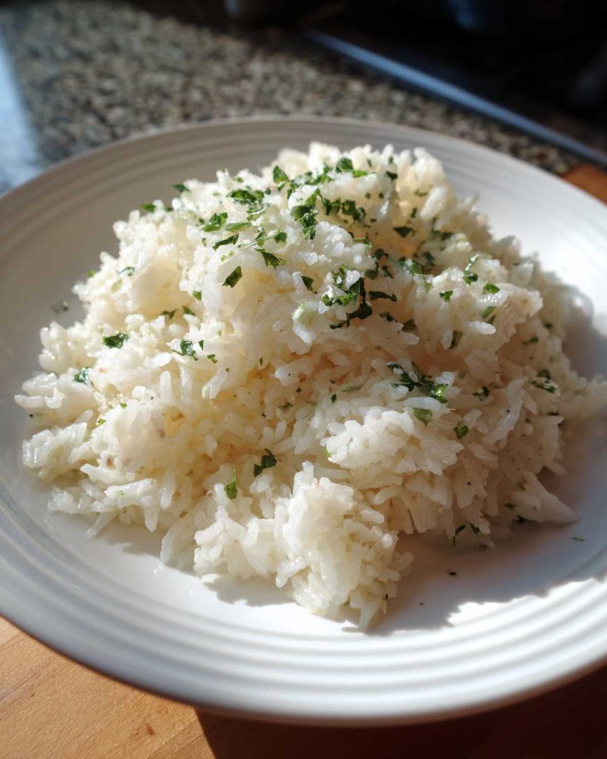 A mound of fluffy white butter rice garnished with chopped green parsley on a white plate.