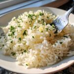 Close-up of fluffy white butter rice mixed with melted butter and topped generously with chopped fresh parsley.