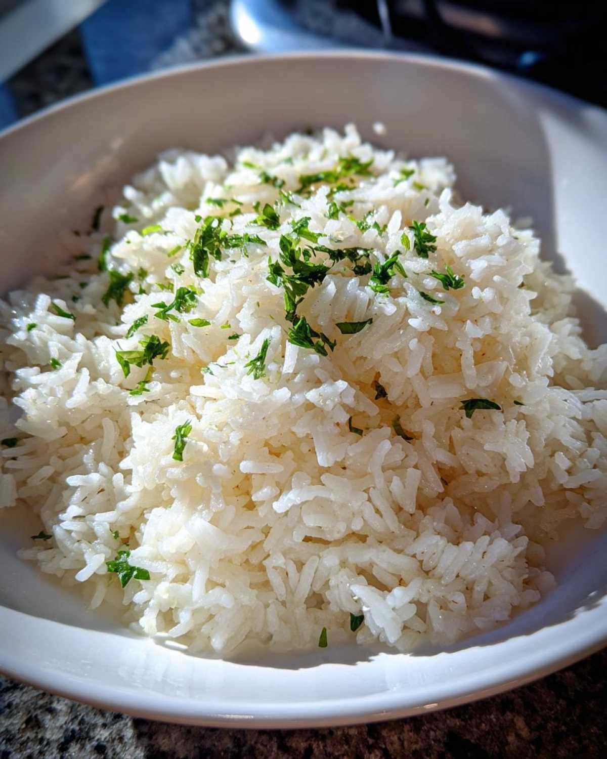 Close-up of fluffy white butter rice served in a white bowl and garnished with chopped green parsley.