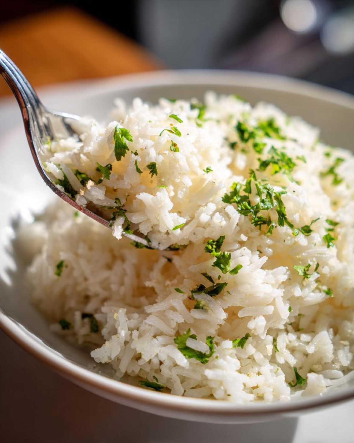 A close-up of fluffy white butter rice topped with fresh parsley, with a fork scooping some out of a white bowl.