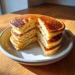 A stack of fluffy coconut flour pancakes with a wedge cut out, showing the light, airy interior texture.