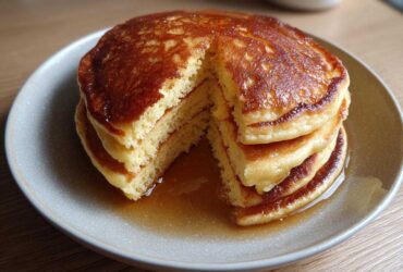 A stack of fluffy coconut flour pancakes with a piece cut out, drizzled generously with maple syrup.