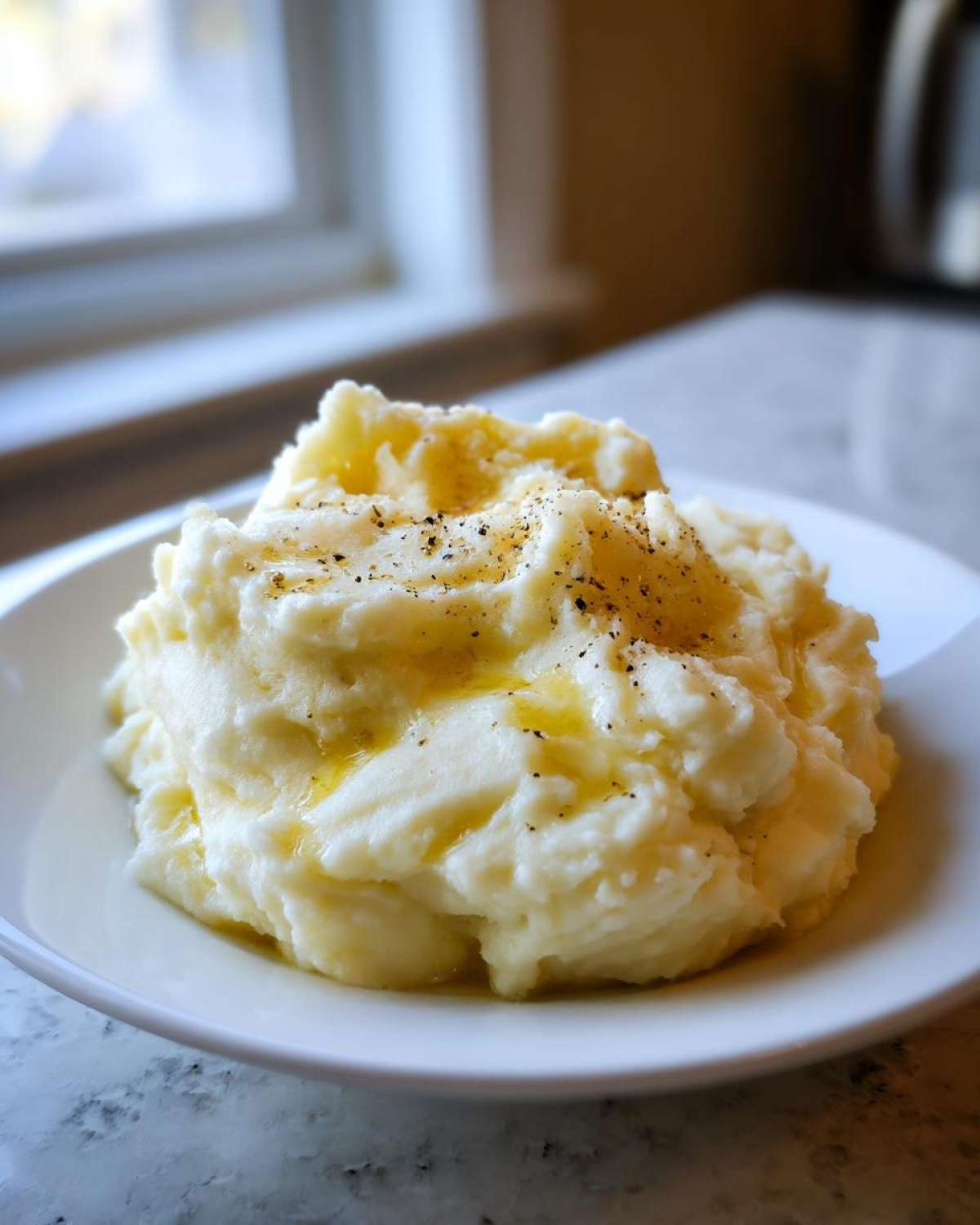 A generous serving of creamy, fluffy mashed potatoes topped with melted butter and freshly cracked black pepper.