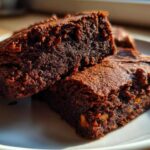 Close-up of two fudgy gingerbread brownies stacked on a white plate, showing rich dark texture.