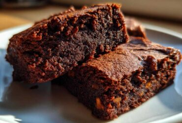 Close-up of two fudgy gingerbread brownies stacked on a white plate, showing rich dark texture.