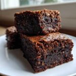 Close-up of three fudgy gingerbread brownies stacked on a white plate, showing a rich, dark texture.