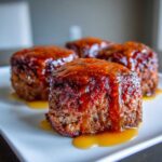 Close-up of four individual mini meatloaf portions topped with a thick, shiny glaze, resting on a white platter.