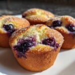 Four golden Gluten-Free Blueberry Lemon Muffin Tops topped with coarse sugar and bursting with blueberries.