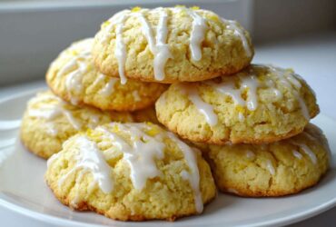 A stack of soft, yellow Gluten-Free Lemon Ricotta Cookies drizzled with white lemon glaze and topped with zest.