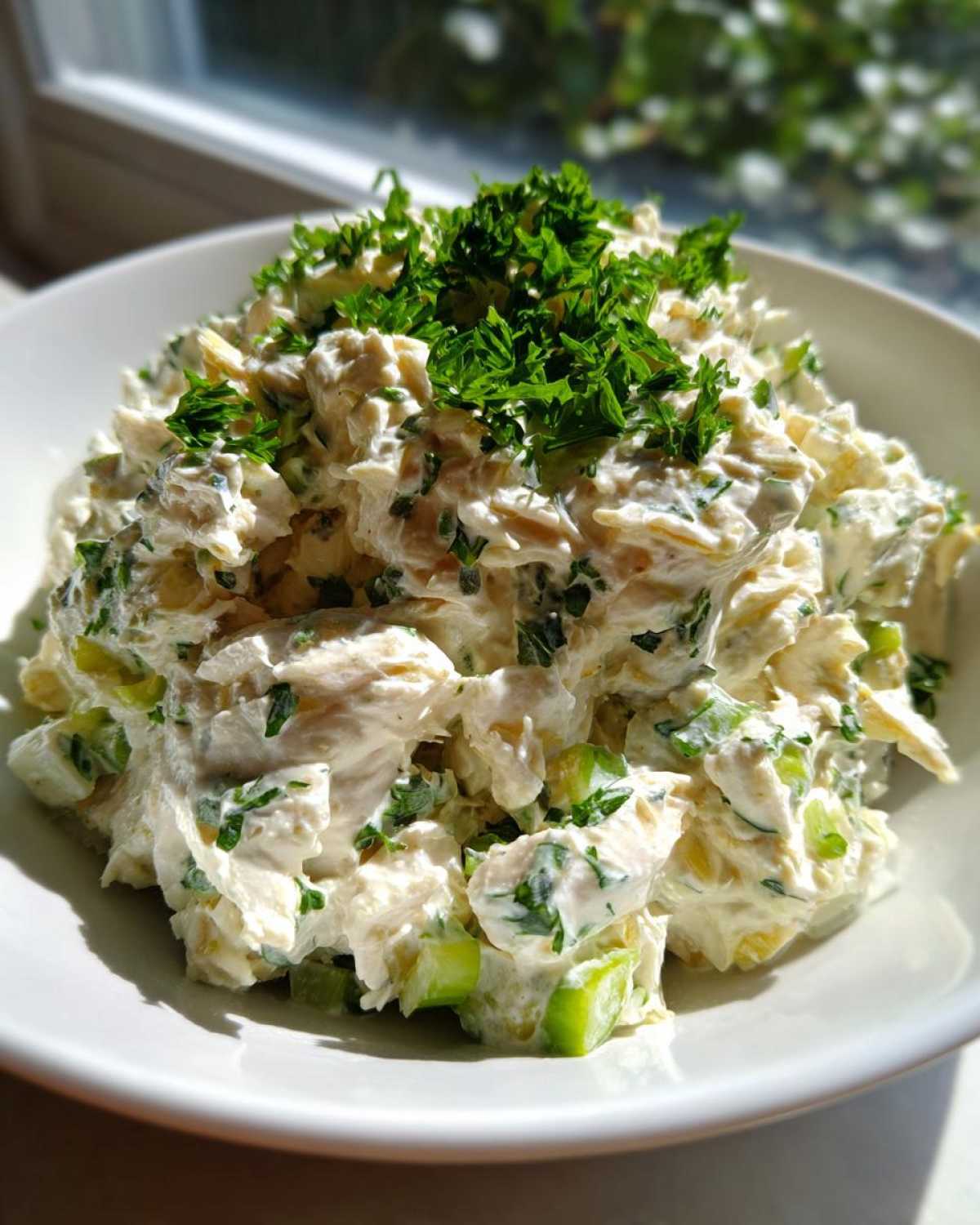 Close-up of creamy greek yogurt chicken salad topped generously with fresh chopped parsley in a white bowl.