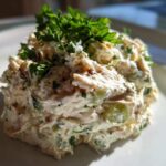 A close-up of a scoop of creamy greek yogurt chicken salad, garnished generously with fresh parsley.