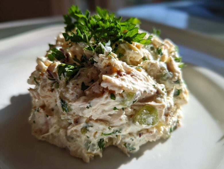 A close-up of a scoop of creamy greek yogurt chicken salad, garnished generously with fresh parsley.