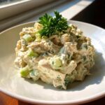 A mound of creamy greek yogurt chicken salad mixed with celery and topped with fresh parsley.