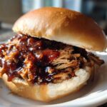 Close-up of a juicy Instant Pot BBQ Pulled Chicken Sandwich piled high on a soft bun with rich sauce.