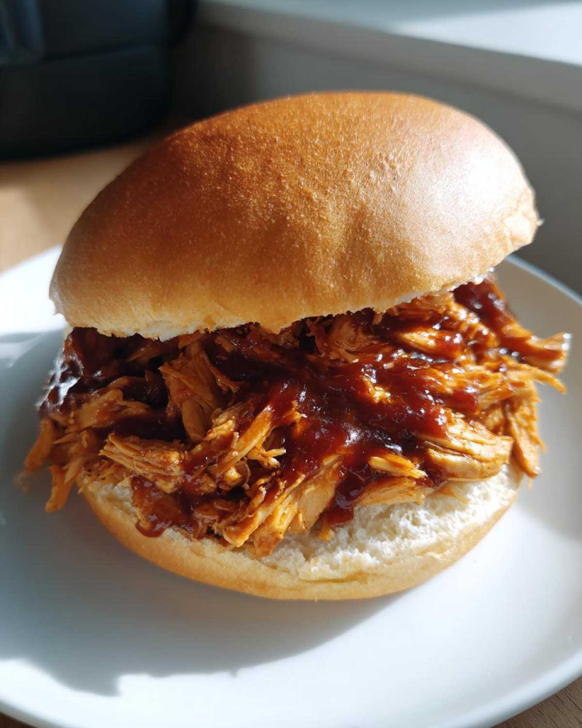 A close-up of a delicious Instant Pot BBQ Pulled Chicken Sandwich served on a white plate.