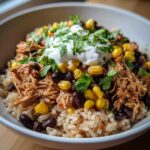 Close-up of Instant Pot Chicken Burrito Bowls with brown rice, shredded chicken, black beans, corn, and sour cream.