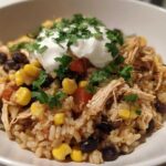 A close-up of Instant Pot Chicken Burrito Bowls with brown rice, shredded chicken, corn, black beans, and sour cream.