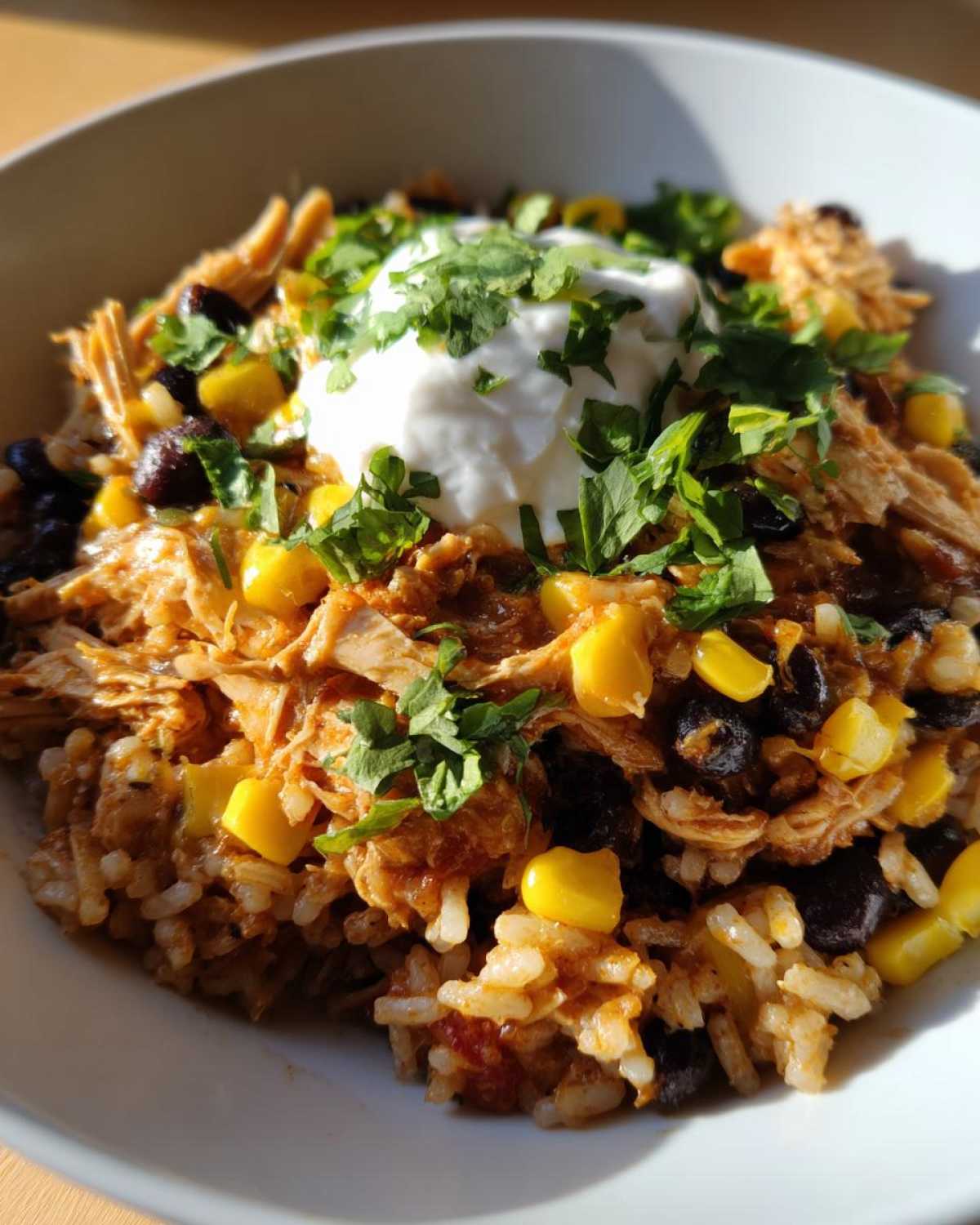 Close-up of Instant Pot Chicken Burrito Bowls with brown rice, black beans, corn, and sour cream topping.