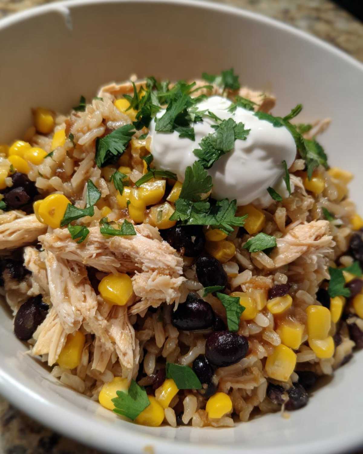 Close-up of Instant Pot Chicken Burrito Bowls with brown rice, shredded chicken, black beans, corn, and sour cream.