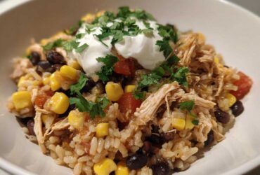 A close-up of Instant Pot Chicken Burrito Bowls with brown rice, shredded chicken, corn, black beans, and sour cream.