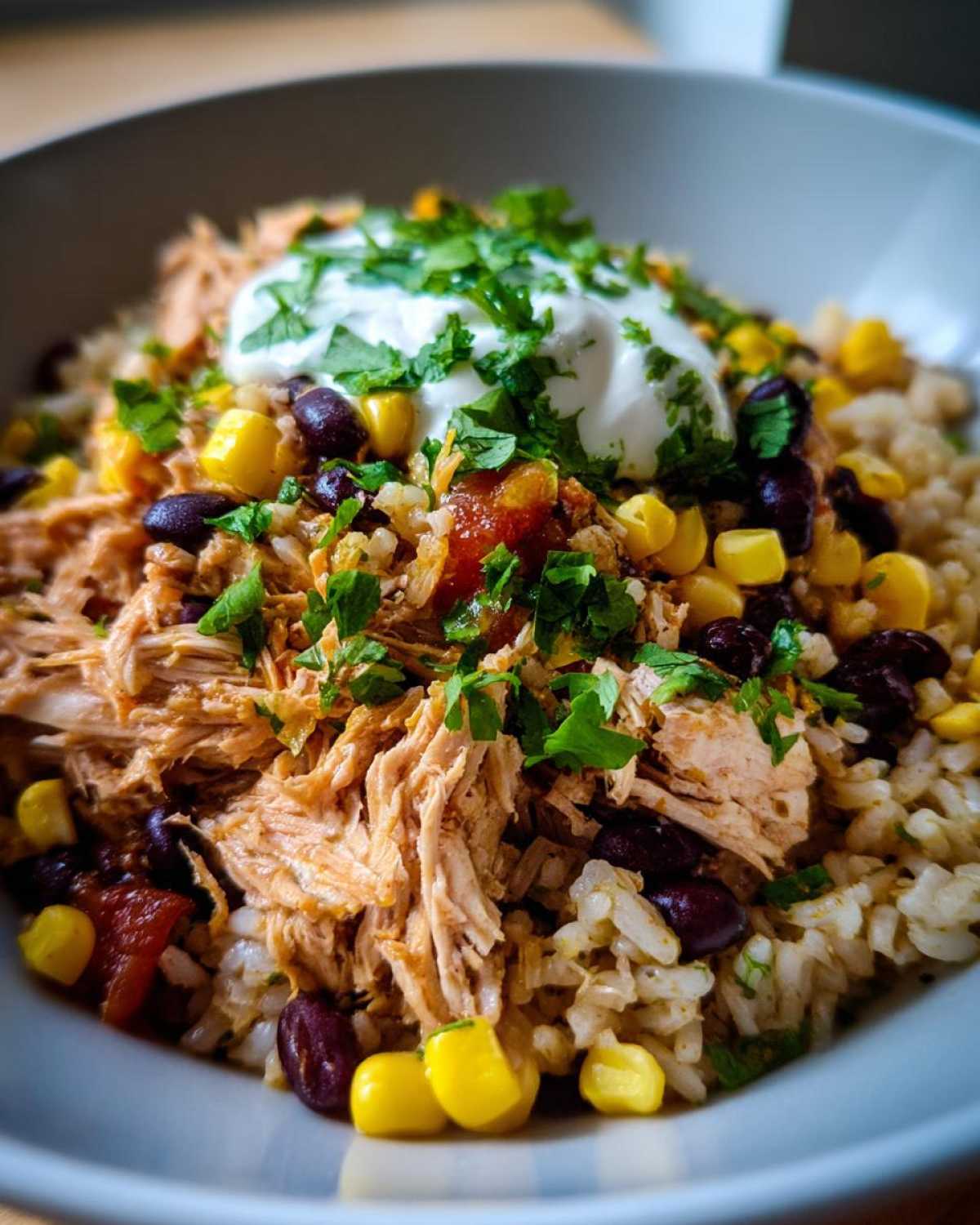 A close-up of Instant Pot Chicken Burrito Bowls featuring shredded chicken, brown rice, black beans, corn, salsa, and sour cream topped with cilantro.