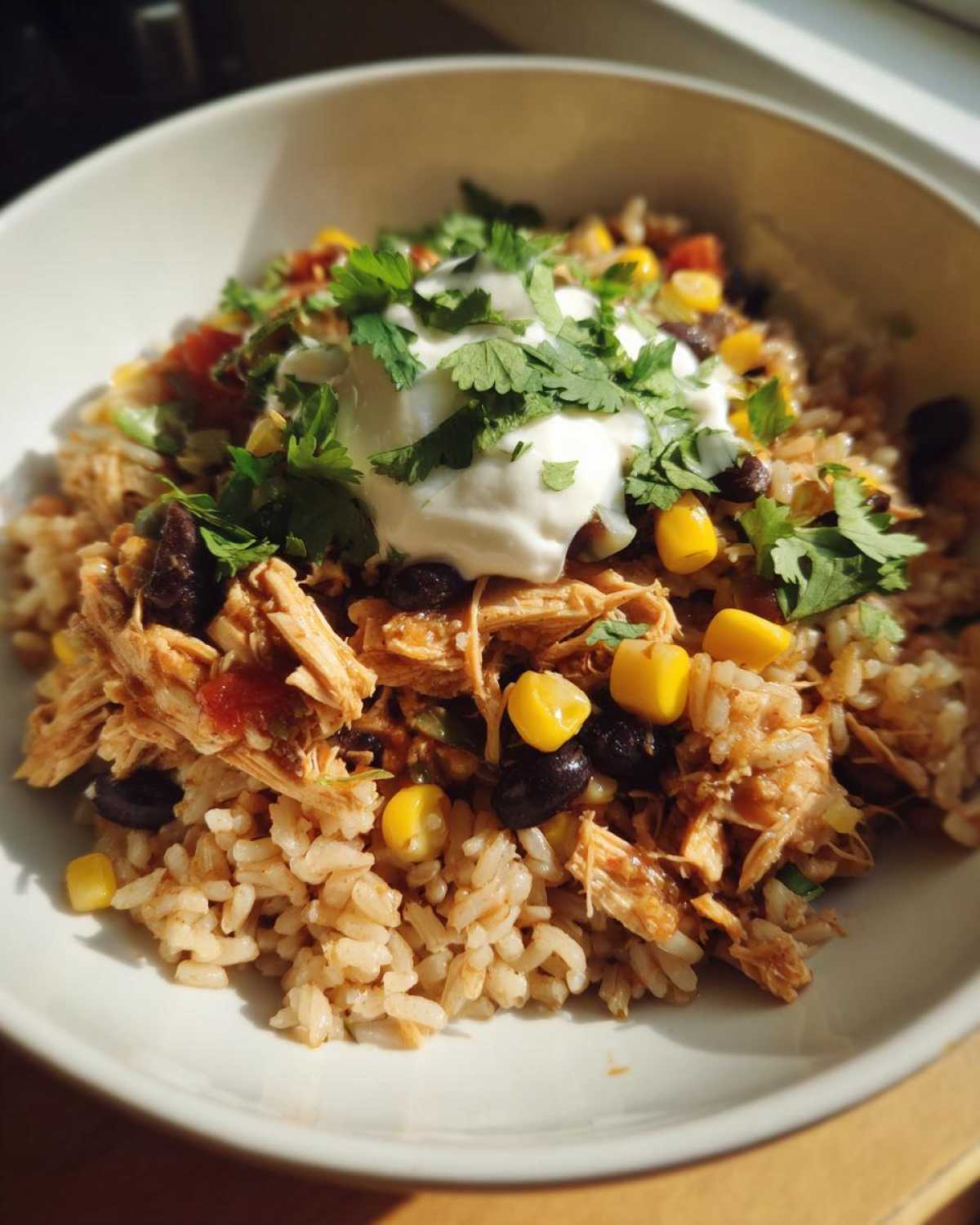 A close-up of Instant Pot Chicken Burrito Bowls with brown rice, shredded chicken, black beans, corn, and sour cream topped with cilantro.