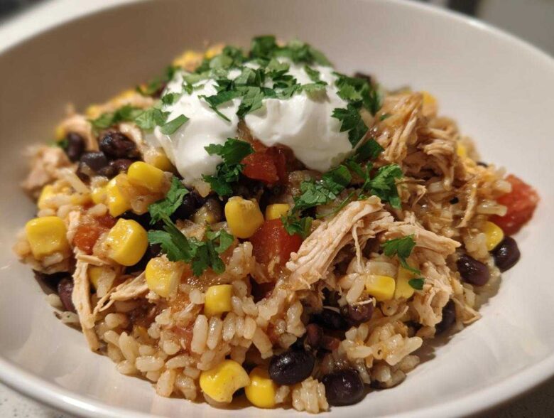 A close-up of Instant Pot Chicken Burrito Bowls with brown rice, shredded chicken, corn, black beans, and sour cream.