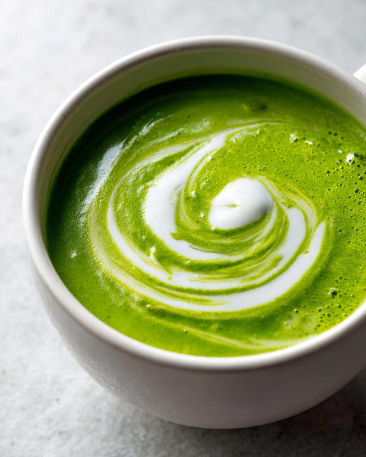 Close-up of vibrant green Instant Pot Creamy Asparagus Soup topped with a white cream swirl.