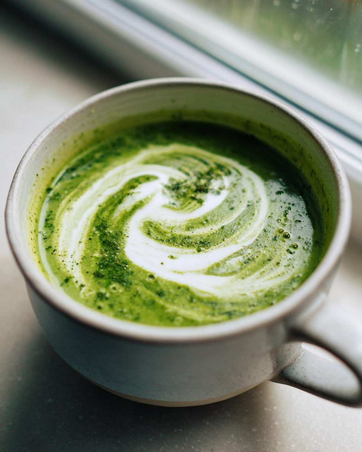 Close-up of a vibrant green Instant Pot Creamy Asparagus Soup with a white cream swirl garnish.