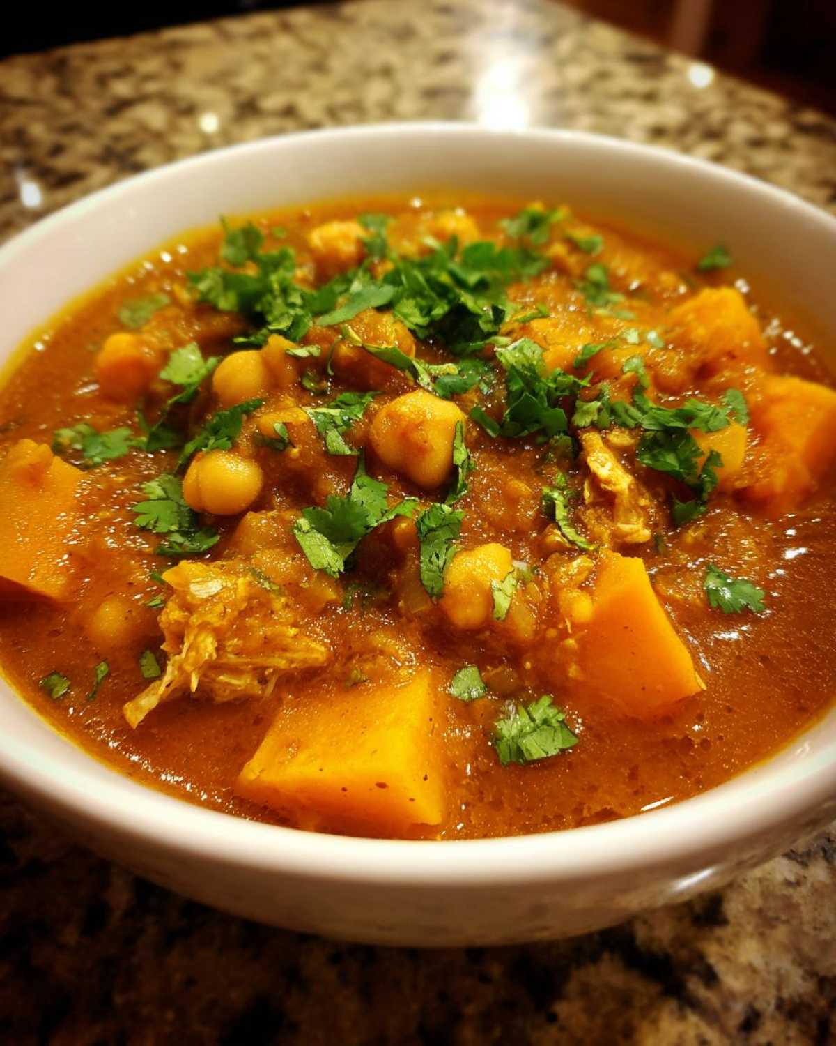 Close-up of a bowl of rich, orange Instant Pot Moroccan Chickpea Stew with sweet potatoes and fresh cilantro garnish.