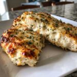 Close-up of two pieces of juicy baked ranch chicken topped with melted, browned cheese and green herbs.