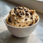 A close-up of thick Keto Chocolate Chip Cookie Dough Dip topped with mini chocolate chips in a white bowl.
