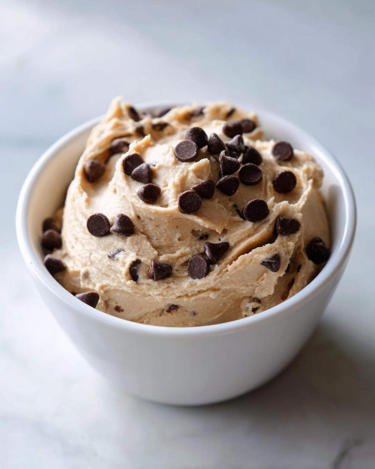 A close-up of thick, creamy Keto Chocolate Chip Cookie Dough Dip topped with mini chocolate chips in a white bowl.