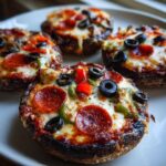 Four baked Keto Pizza Stuffed Portobello Mushrooms topped with melted cheese, pepperoni, olives, and peppers on a white plate.