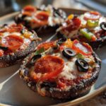 Four baked Keto Pizza Stuffed Portobello Mushrooms topped with melted cheese, pepperoni, olives, and peppers.