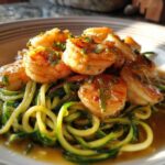 A close-up of Keto Shrimp Scampi Zucchini Noodles, featuring plump shrimp over green zucchini spirals in a buttery sauce.