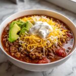 A close-up of a hearty bowl of Keto Taco Soup with Ground Beef, topped with avocado slices, shredded cheese, and sour cream.