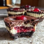 Close-up of a No-Bake Chocolate Cherry Cheesecake Cup with a bite taken out, showing layers of crust, cream cheese, cherry filling, and chocolate topping.
