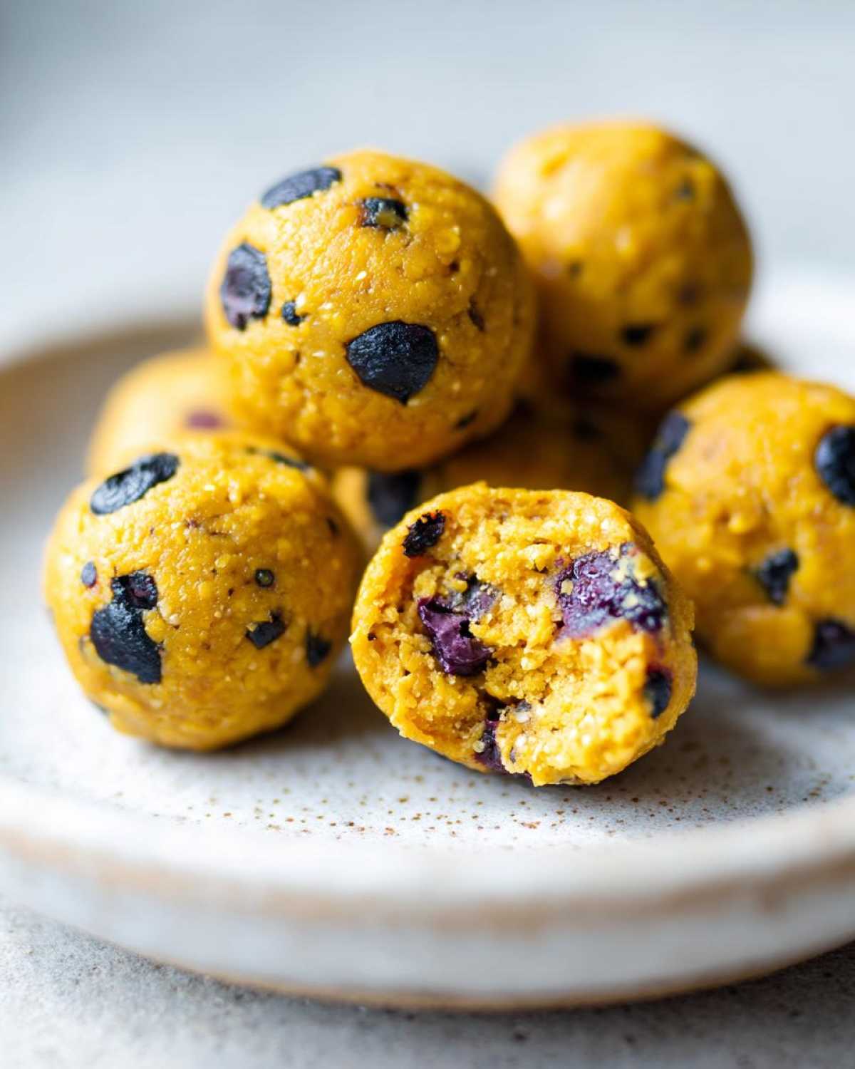 Close-up of bright yellow No-Bake Lemon Blueberry Energy Bites, one is cut open showing blueberries inside.