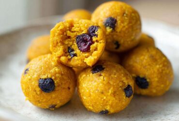 Close-up of vibrant yellow No-Bake Lemon Blueberry Energy Bites, one is broken open showing dried blueberries inside.