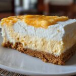 A close-up of a layered No-Bake Orange Creamsicle Cheesecake Bars slice on a white plate.