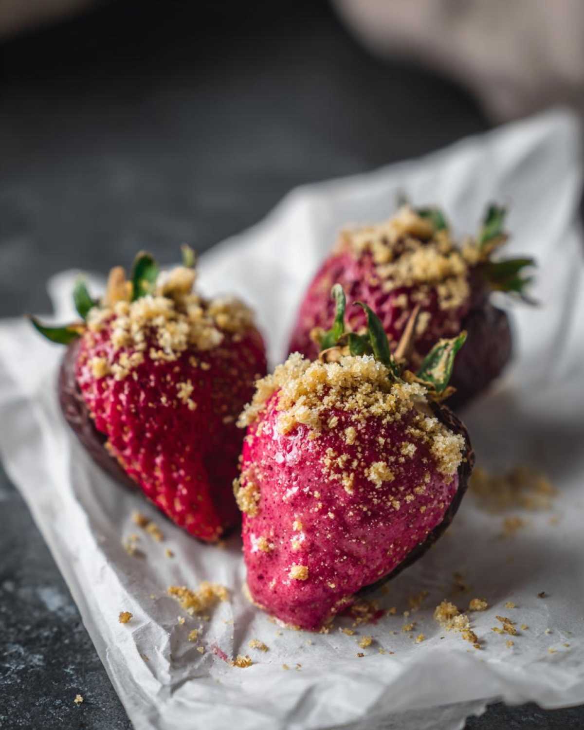 Three No-Bake Strawberry Cheesecake Stuffed Dates topped with graham cracker crumbs on parchment paper.