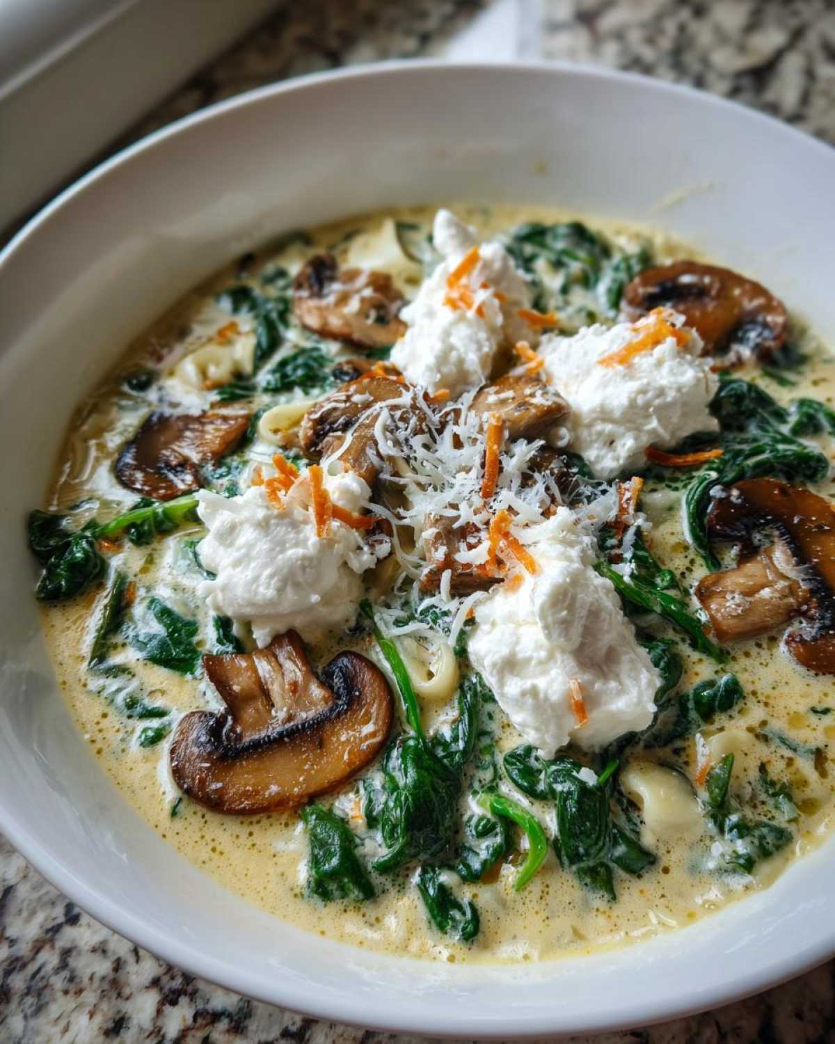 A close-up bowl of One-Pot Creamy Spinach Mushroom Lasagna Soup topped with dollops of ricotta and grated cheese.