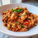 A close-up of One-Pot Creamy Tomato Basil Chicken and Rice served in a white bowl, garnished with fresh basil.